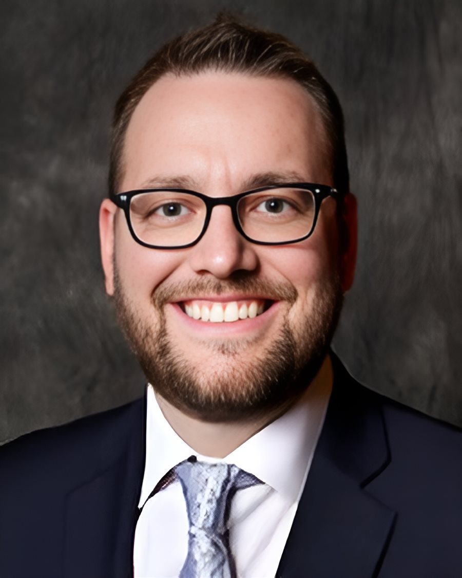 Portrait of Mark McKenzie, smiling, wearing a dark suit and glasses