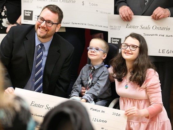 Mark McKenzie with two young Easter Seals ambassadors, holding donation cheques totalling $124,000